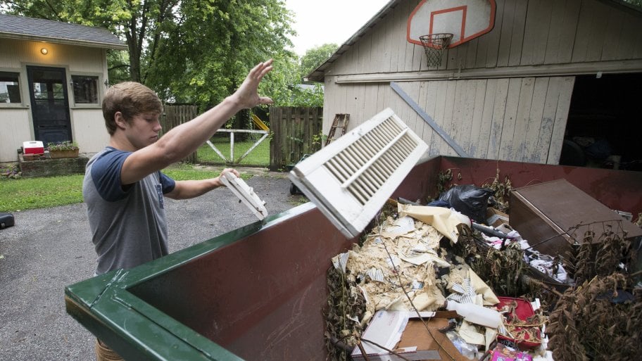 A man tossing junk into a dumpster